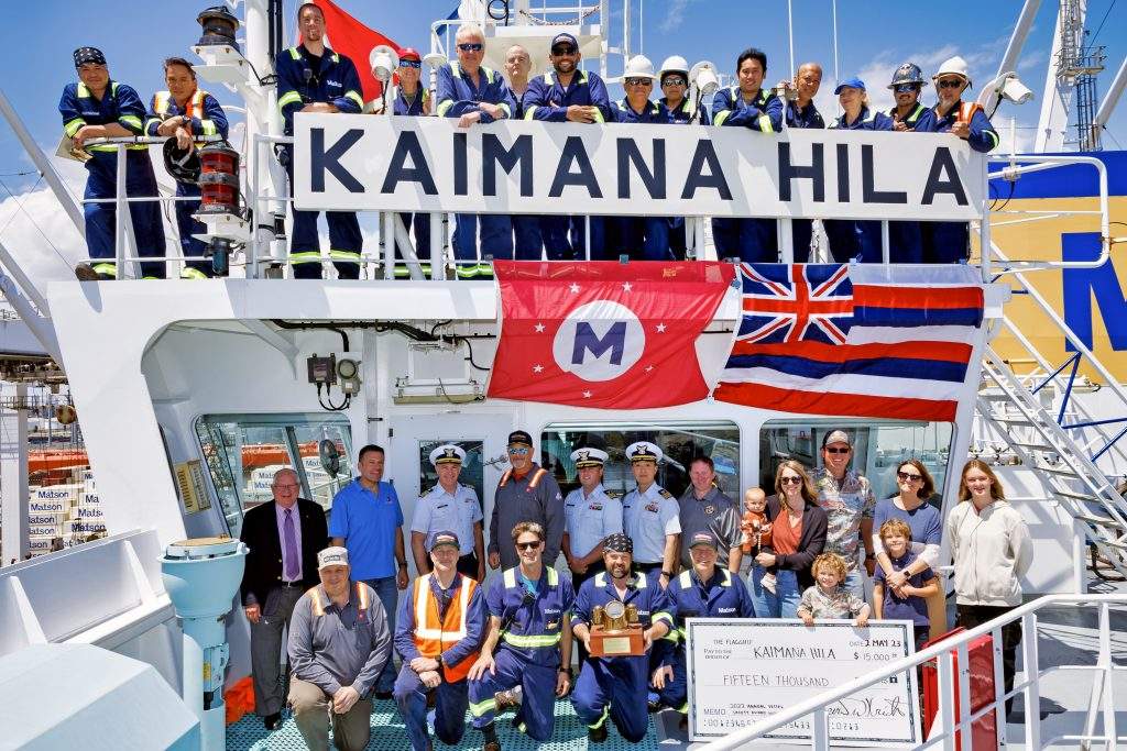 Kaimana Hila crew gather on top and in front of the bridge with the vessel name board, Matson and Hawaii state flags, and presentation check.