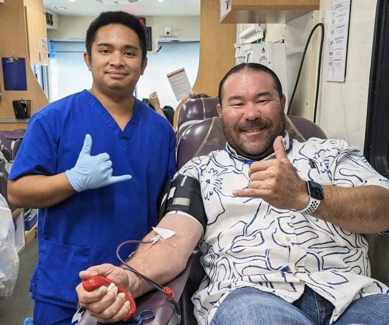 Blood bank staff and Matson blood donor smile and give shakas during a donation.