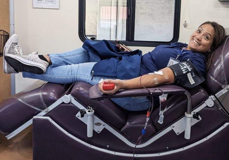 Donor lays in the chair and smiles for the camera as tubing connects her arm to the bag of blood.