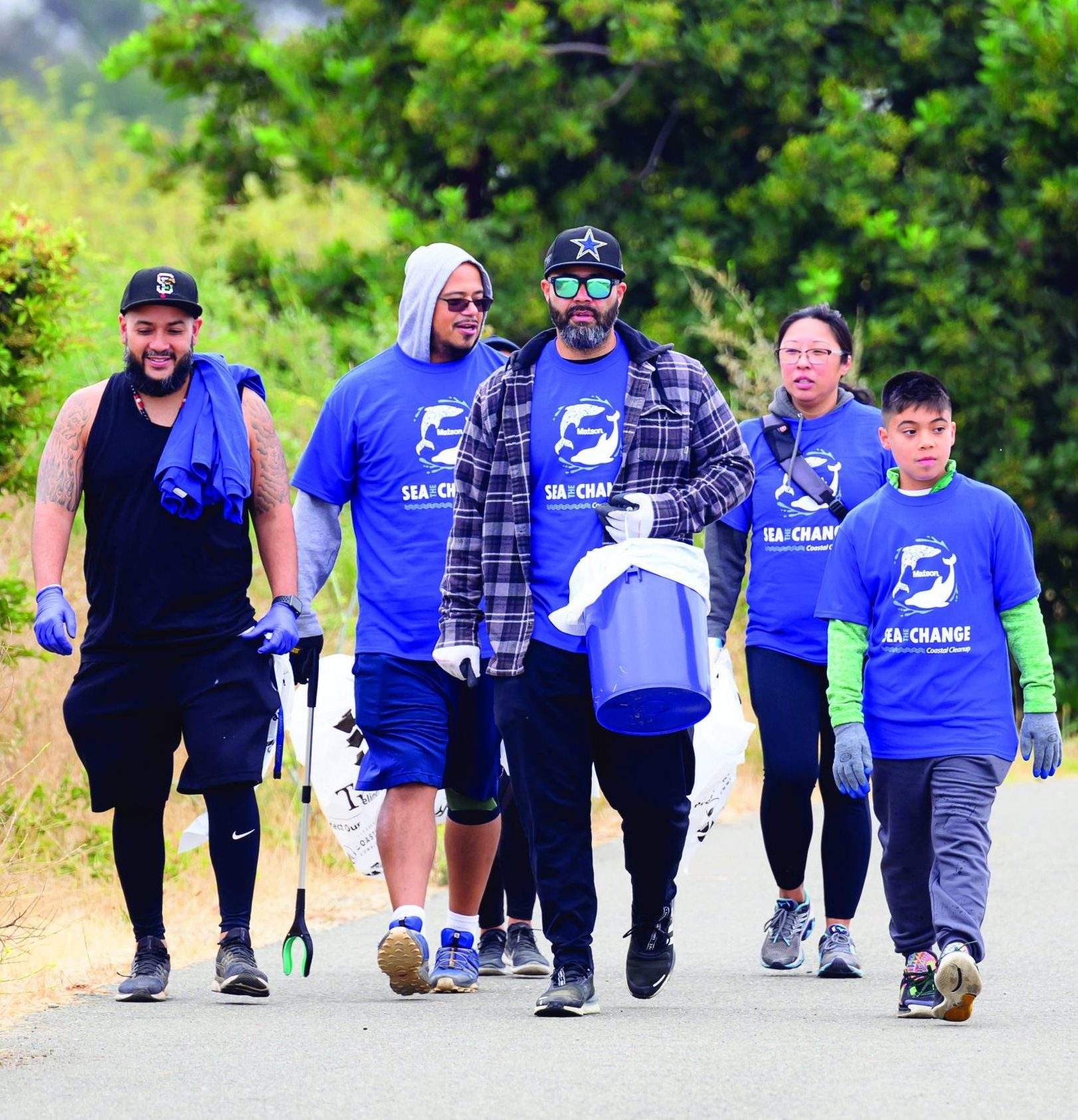Group of volunteers wearing blue Matson "Sea The Change" t-shirts and equipped with grabbers, bags and a bucket, walk to the clean-up area.