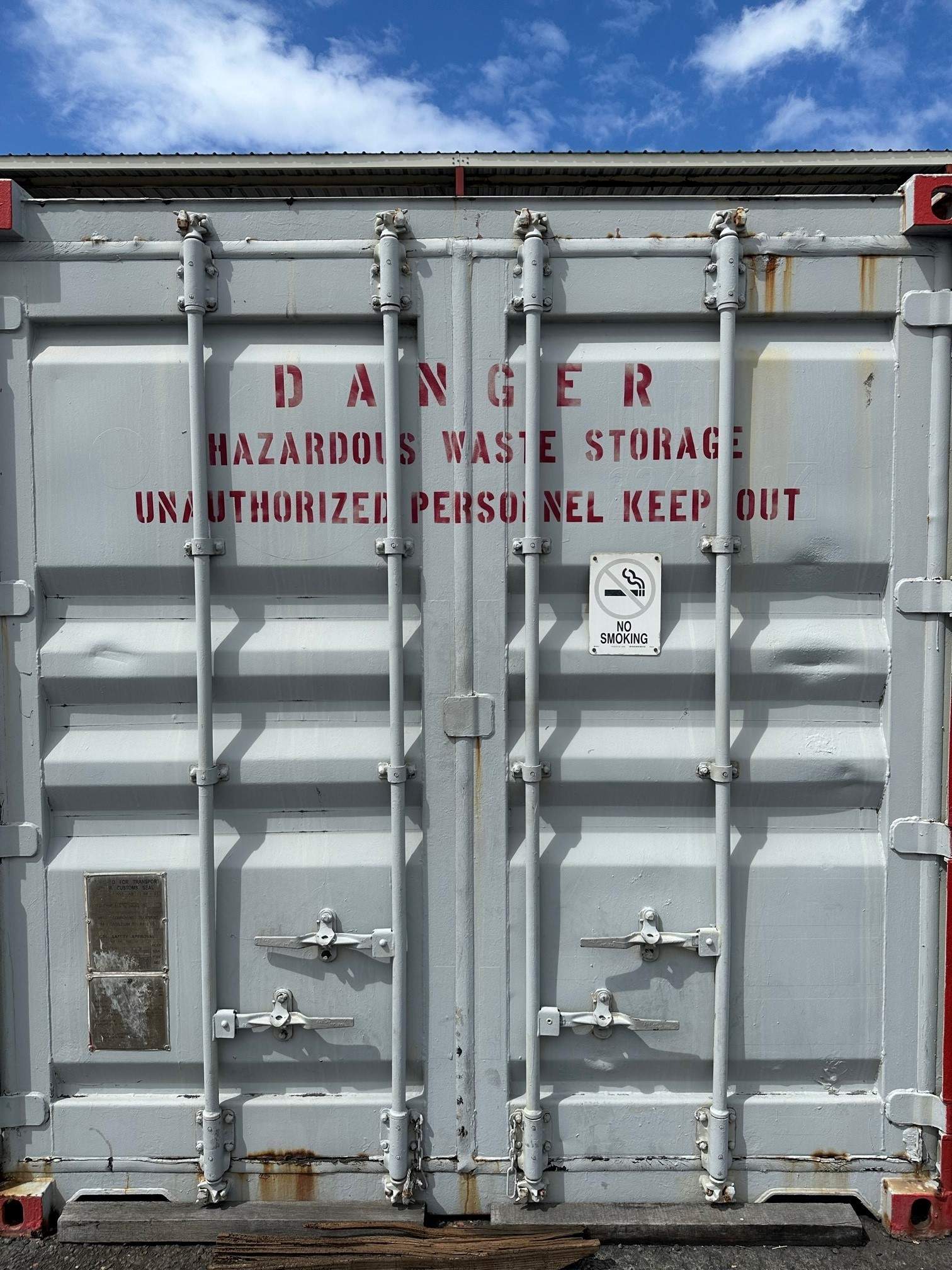 Gray container marked "DANGER Hazardous Waste Storage Unauthorized Personnel Keep Out" in red sits at a terminal.