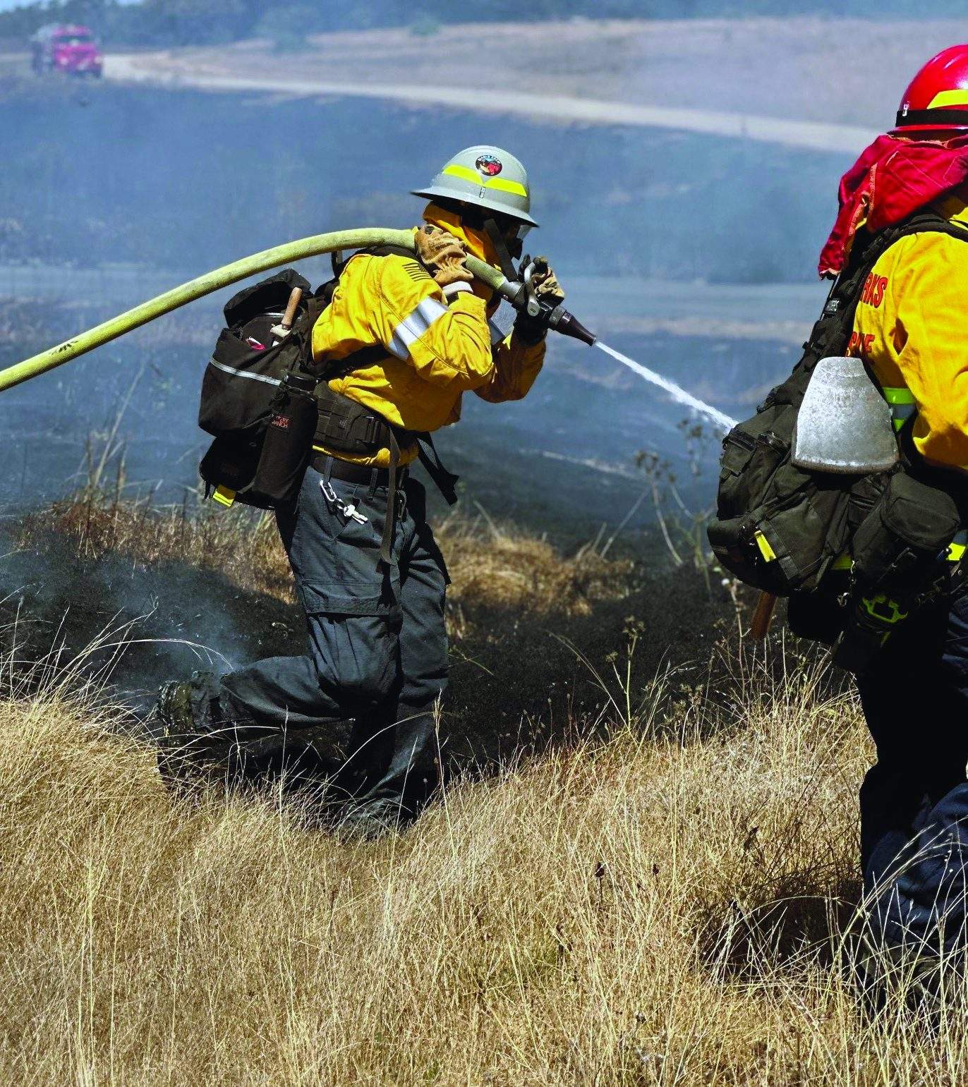 Erica Bradley holds a hose over her shoulder as she helps extinguish a grassfire.