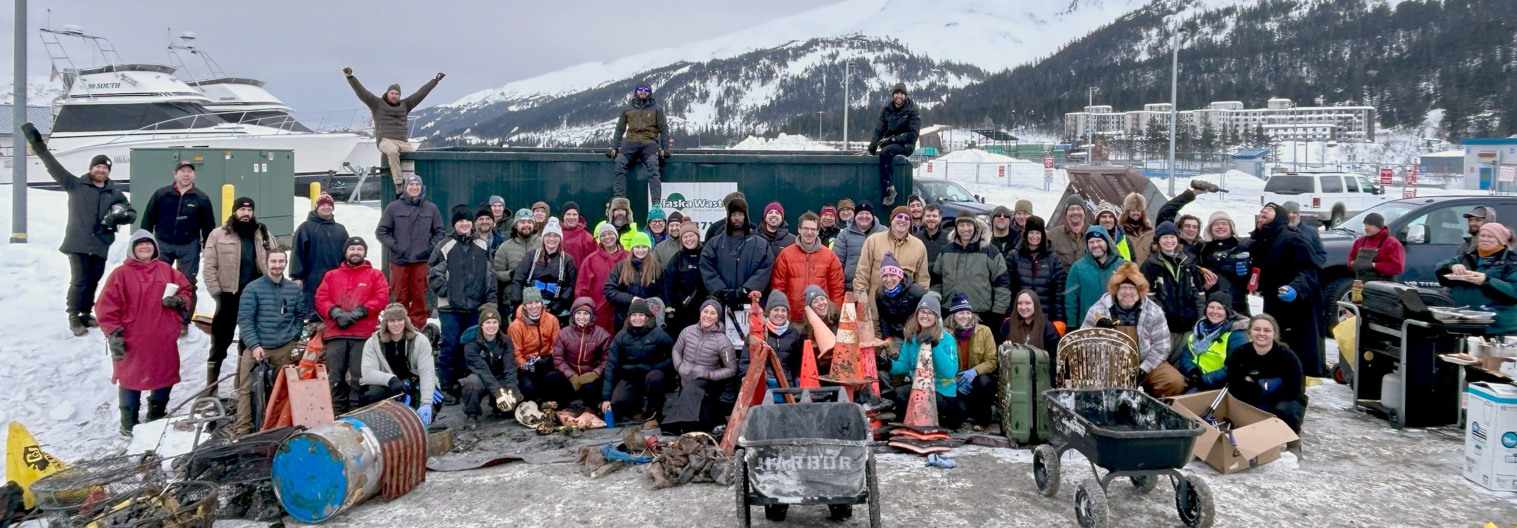 Dive Alaska volunteers bundled in warm clothes pose in a group photo with the objects they've retrieved from the water.