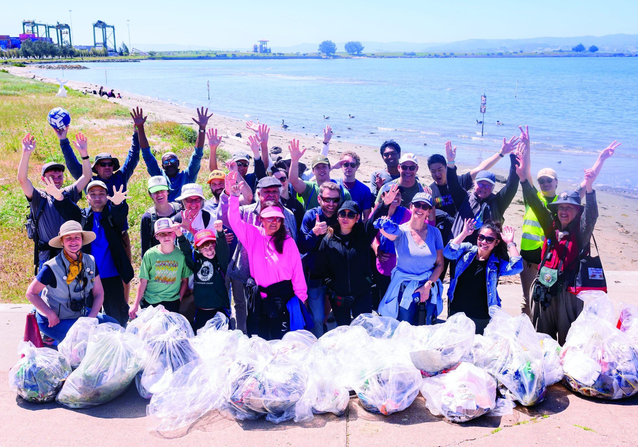 Volunteers stand on the Oakland shoreline with full bags of trash.