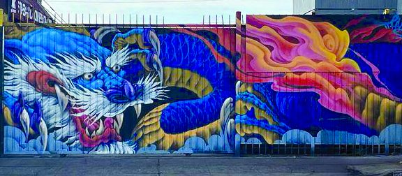 Mural of a blue dragon with white whiskers decorates a fence.