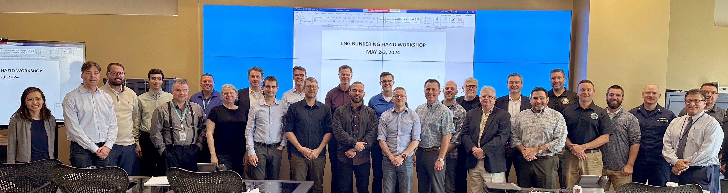 Workshop attendees stand in a conference room in front of a large screen.
