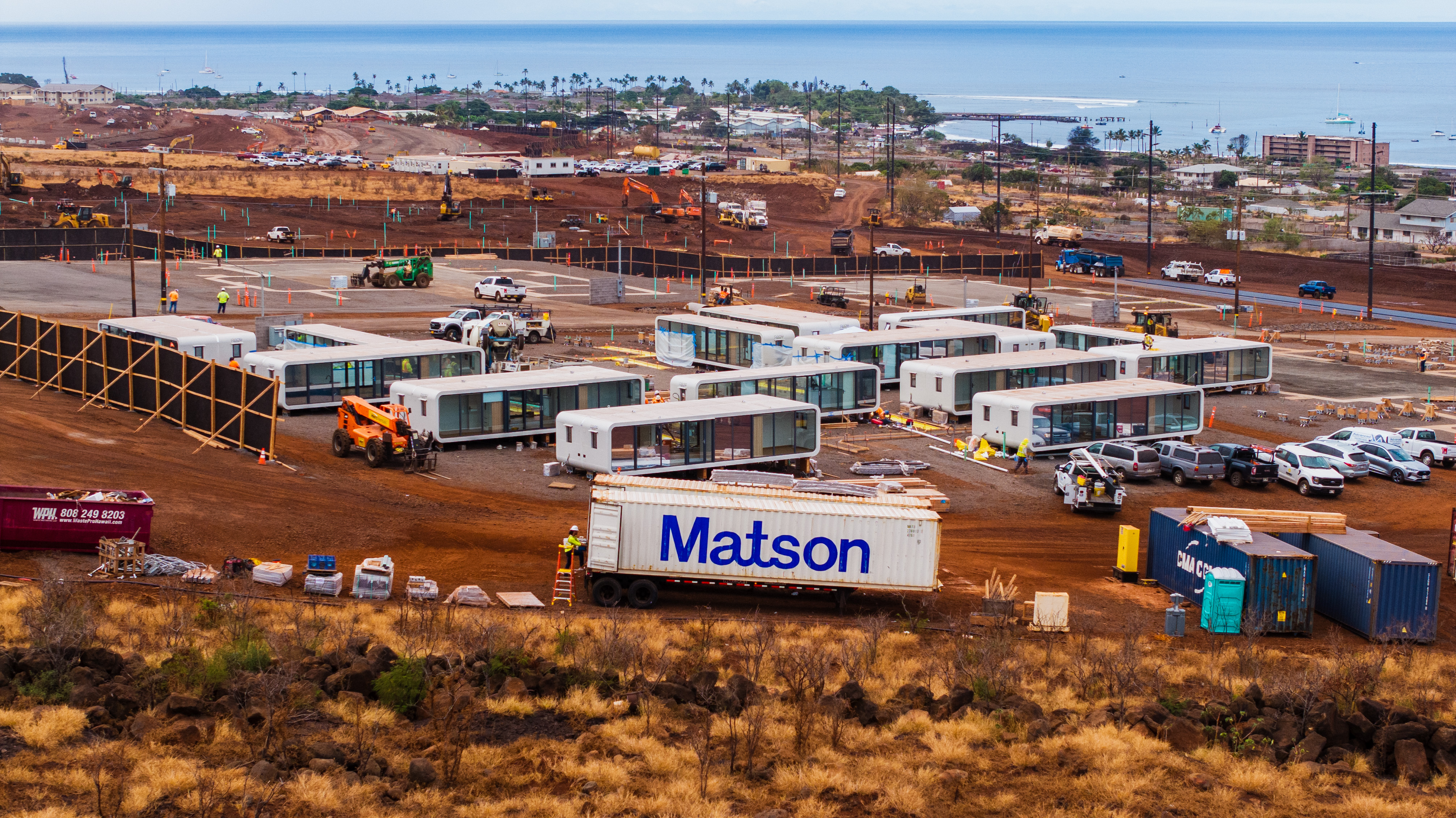 A Matson container sits on the development site of a temporary housing project in Lahaina with the ocean in the background.