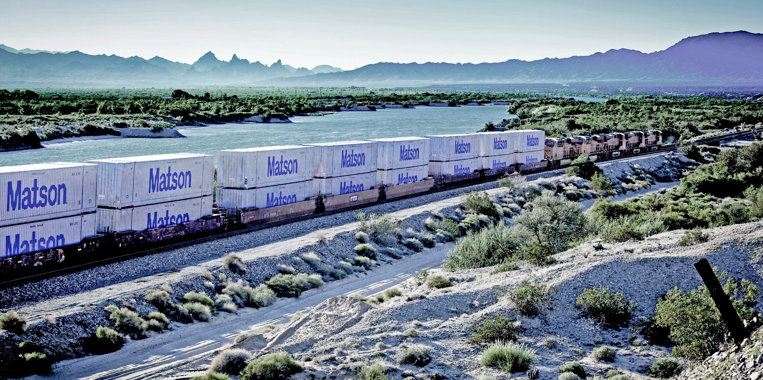 Matson Logistics' 53-foot intermodal containers on the rail with a river and mountains in the background.