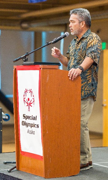 Matson's senior vice president, Alaska, dressed in an aloha shirt, speaks into a microphone behind a podium branded with Special Olympics Alaska.