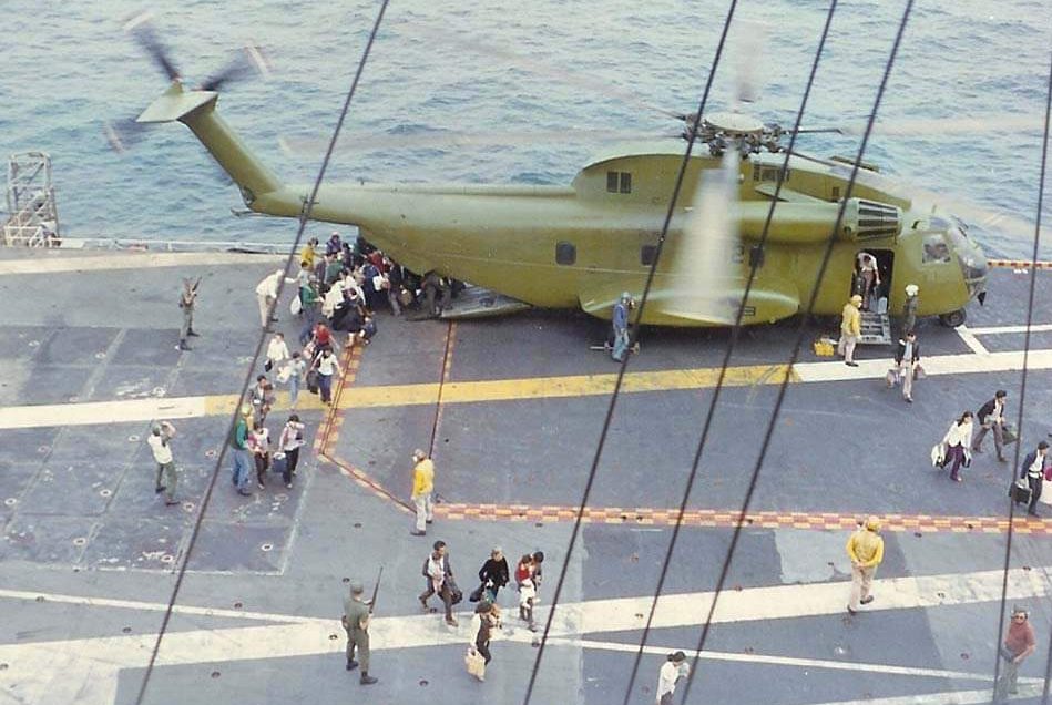 Evacuees carrying little belongings disembark a green Navy helicopter on the deck of the U.S.S. Hancock.